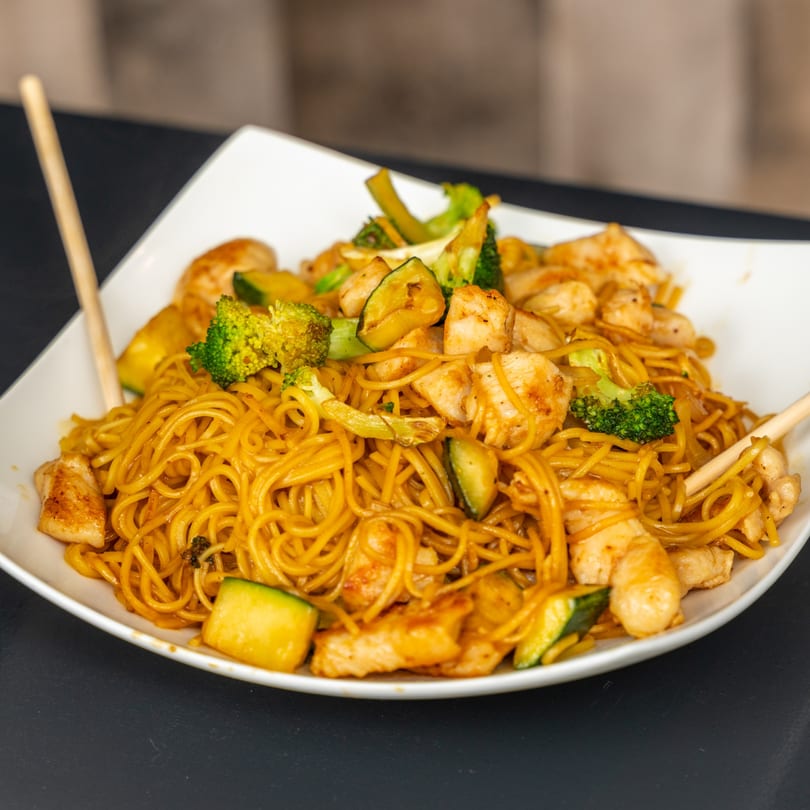 Japanese chicken yakisoba noodles with broccoli and zucchini in a white bowl with chopsticks.