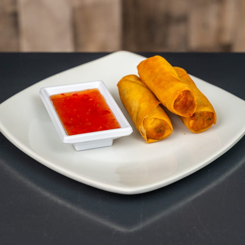 Three crispy golden spring rolls on a white plate with a side of sweet chili dipping sauce.