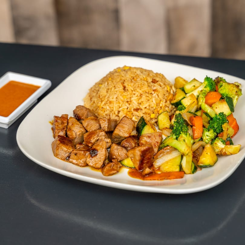 Japanese steak hibachi with fried rice and mixed vegetables on a white plate with dipping sauce.