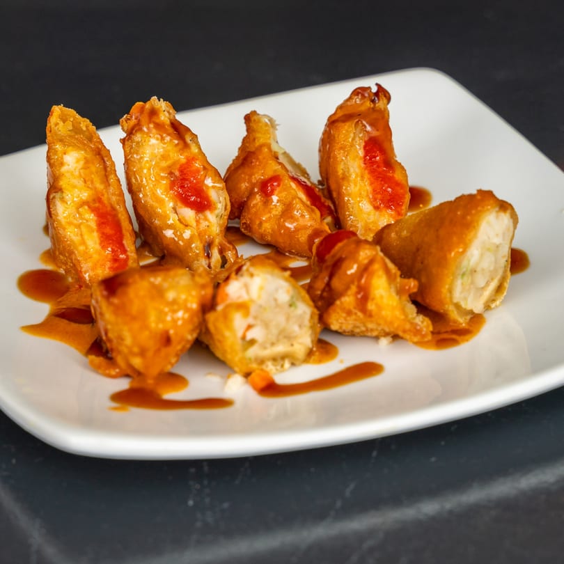 Japanese fried dumplings with orange sauce and red chili paste on a white plate.