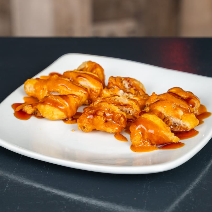 Golden-brown Japanese fried chicken pieces, glistening with sweet orange sauce, on a white plate.