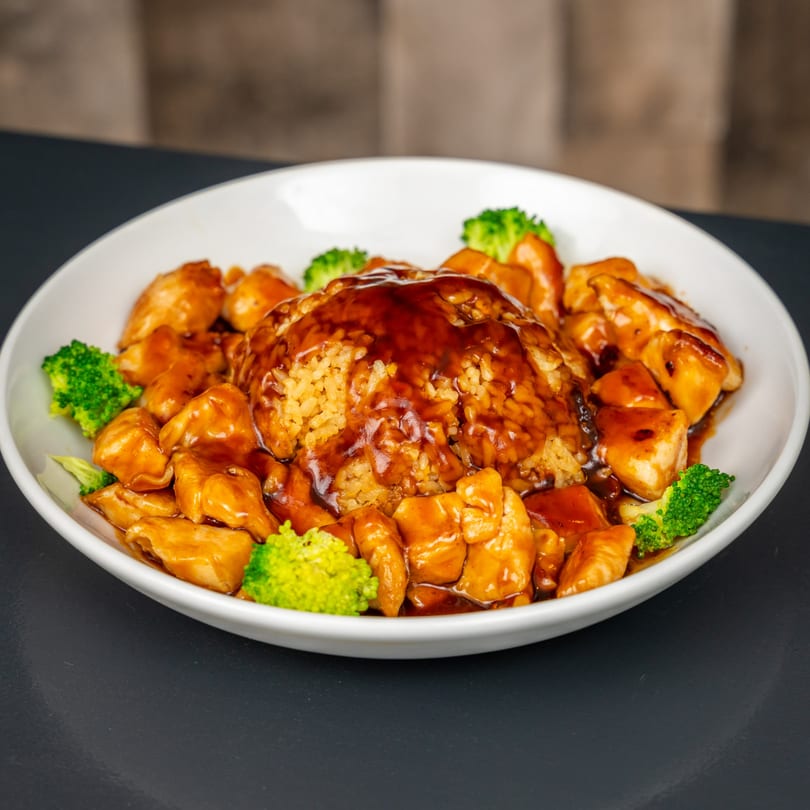 Teriyaki chicken and broccoli with rice, drizzled in sauce, served in a white bowl.